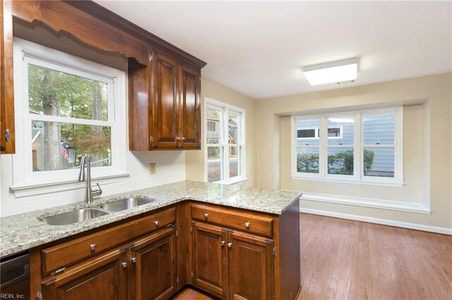 kitchen with dishwasher, kitchen peninsula, sink, light stone countertops, and light wood-type flooring