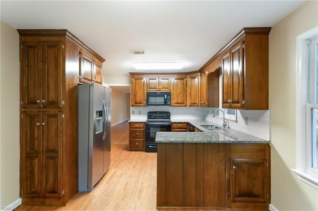 kitchen with light hardwood / wood-style floors, dark stone counters, kitchen peninsula, black appliances, and sink