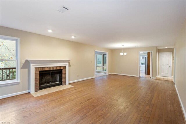 unfurnished living room featuring an inviting chandelier, light hardwood / wood-style floors, and a fireplace