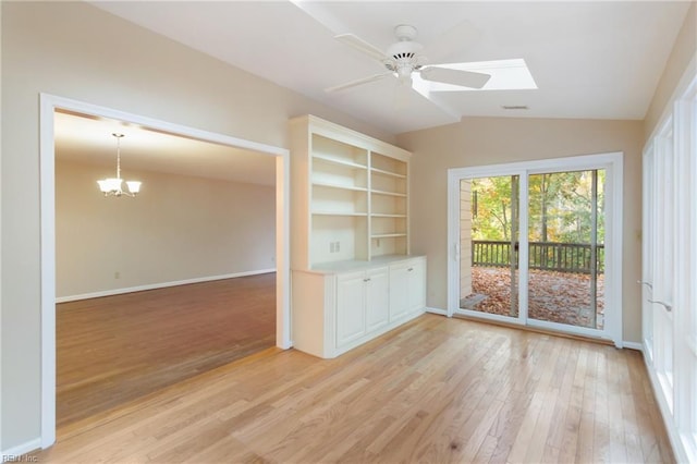 empty room featuring light wood-type flooring, ceiling fan with notable chandelier, and lofted ceiling with skylight