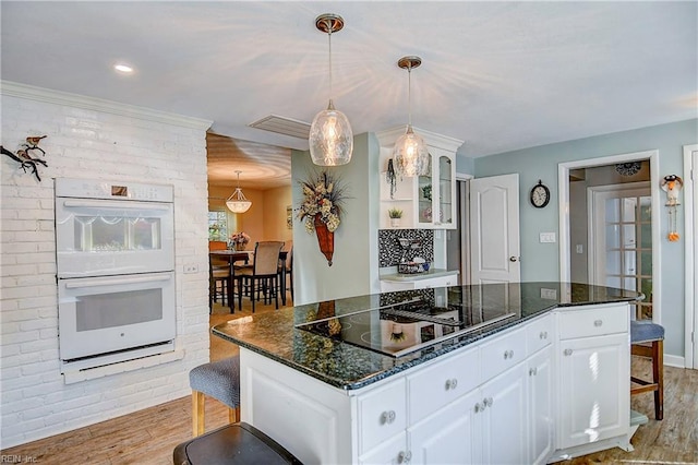 kitchen with black electric stovetop, white cabinetry, light hardwood / wood-style flooring, white double oven, and a center island