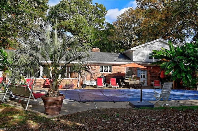 rear view of property featuring a covered pool and a patio area