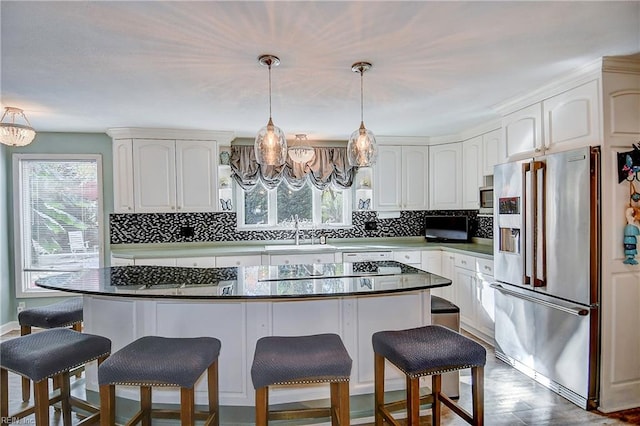 kitchen featuring stainless steel appliances, white cabinetry, tasteful backsplash, decorative light fixtures, and a center island