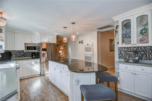 kitchen featuring white cabinetry, appliances with stainless steel finishes, backsplash, decorative light fixtures, and a center island