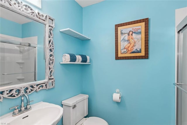 bathroom featuring a shower with shower door, sink, and toilet