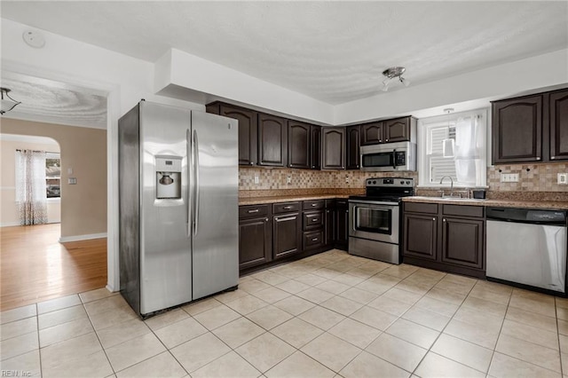 kitchen with stainless steel appliances, dark brown cabinets, light tile patterned floors, and decorative backsplash