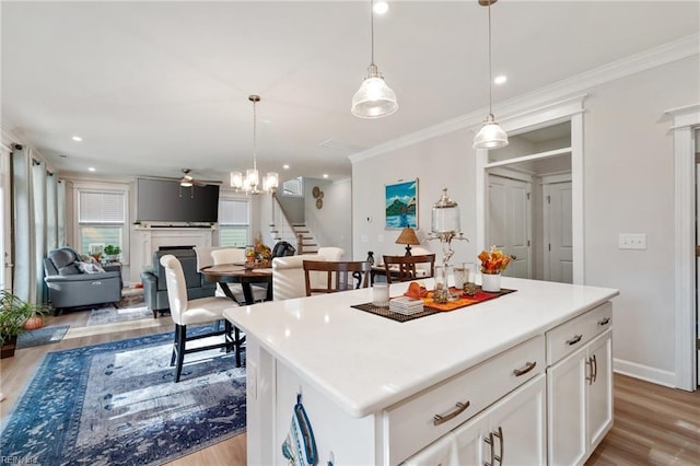 kitchen with ceiling fan, a kitchen island, hanging light fixtures, light wood-type flooring, and white cabinets