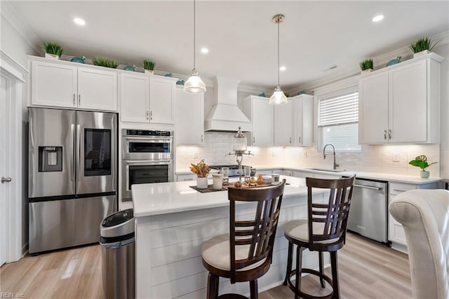 kitchen with custom exhaust hood, appliances with stainless steel finishes, light wood-type flooring, pendant lighting, and white cabinets