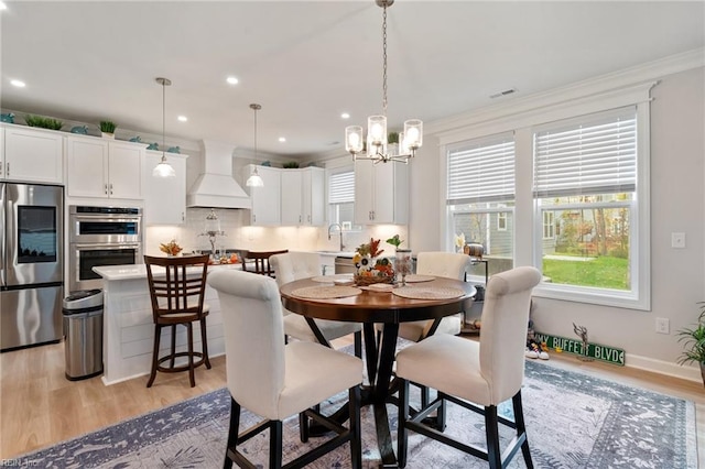 dining space featuring light hardwood / wood-style floors, sink, crown molding, and a chandelier