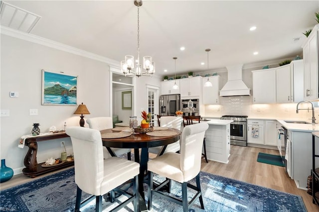 dining space featuring sink, crown molding, a chandelier, and light hardwood / wood-style flooring