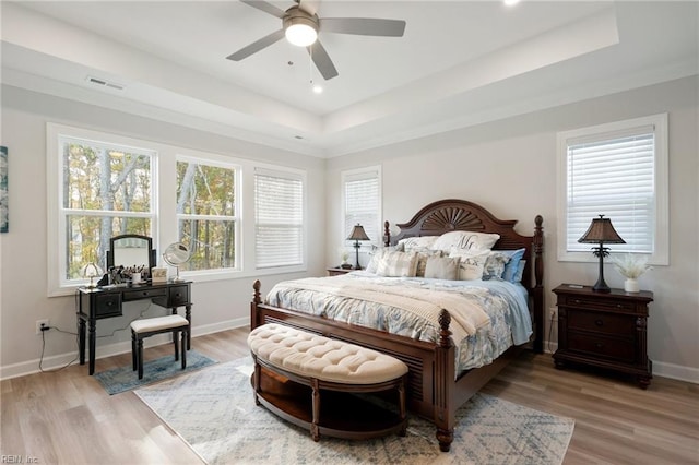 bedroom featuring light wood-type flooring, ceiling fan, a tray ceiling, and multiple windows