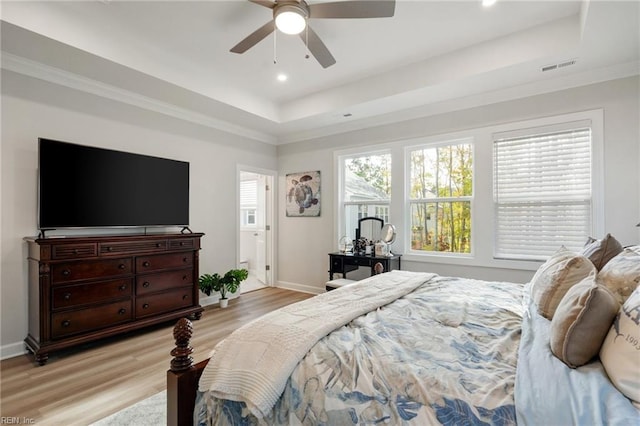 bedroom with ceiling fan, light wood-type flooring, and a tray ceiling