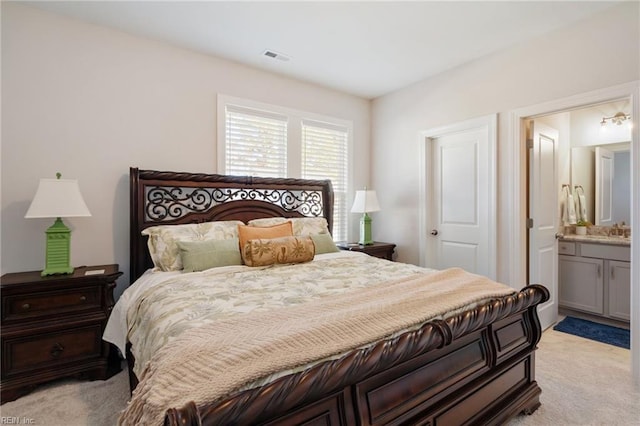 bedroom with ensuite bathroom and light colored carpet