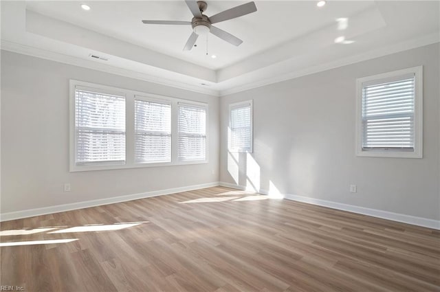 empty room with a raised ceiling, ceiling fan, crown molding, and hardwood / wood-style floors