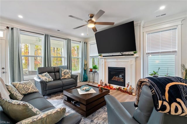 living room featuring ceiling fan, wood-type flooring, crown molding, and a tiled fireplace