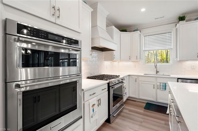 kitchen with decorative backsplash, sink, white cabinetry, light hardwood / wood-style flooring, and stainless steel appliances