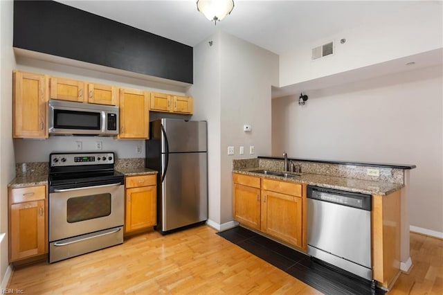 kitchen with appliances with stainless steel finishes, light hardwood / wood-style flooring, light stone counters, and sink