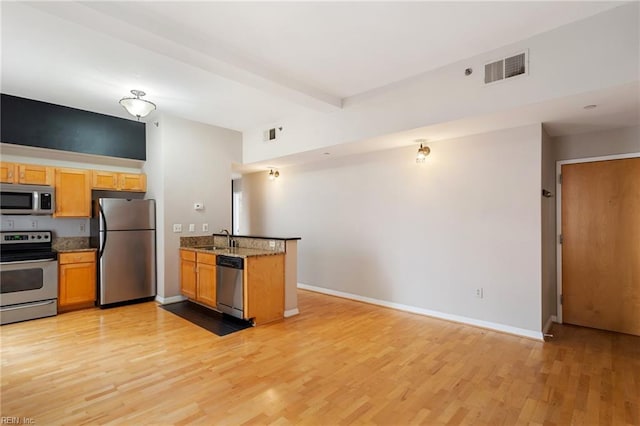 kitchen with light stone countertops, appliances with stainless steel finishes, beamed ceiling, sink, and light wood-type flooring