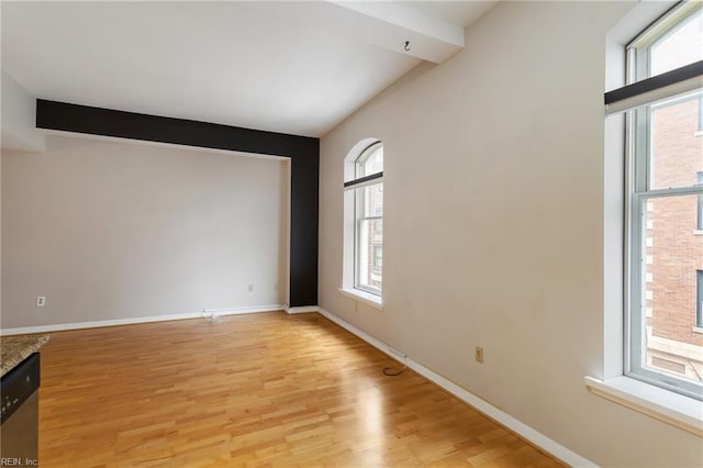 empty room with a wealth of natural light, light hardwood / wood-style flooring, and beamed ceiling