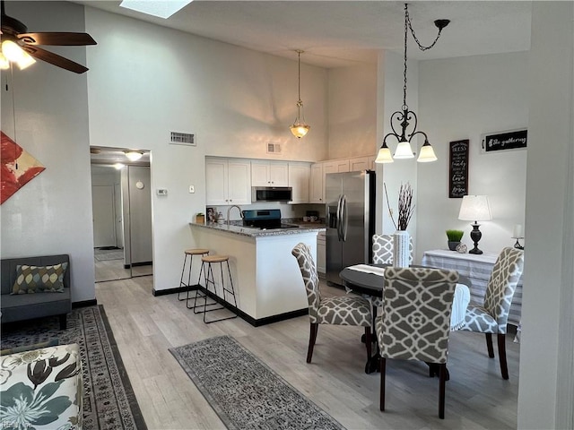 kitchen featuring kitchen peninsula, high vaulted ceiling, white cabinetry, light wood-type flooring, and appliances with stainless steel finishes