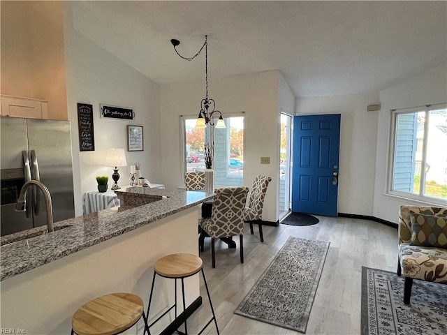 kitchen with light stone countertops, light hardwood / wood-style floors, vaulted ceiling, and stainless steel fridge