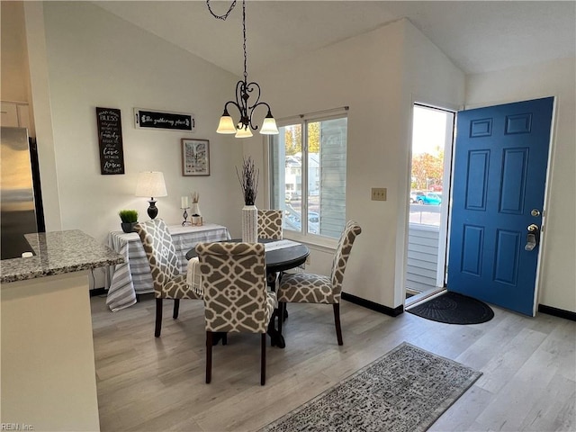 dining space with light wood-type flooring, a chandelier, and vaulted ceiling