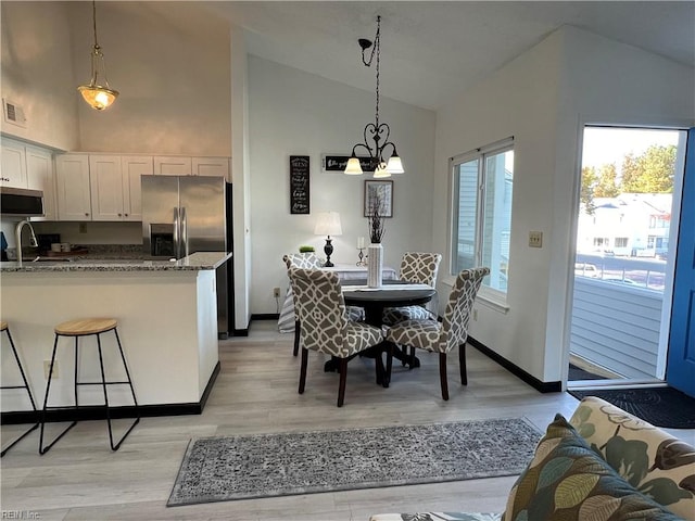 dining area featuring a chandelier, sink, light hardwood / wood-style flooring, and high vaulted ceiling