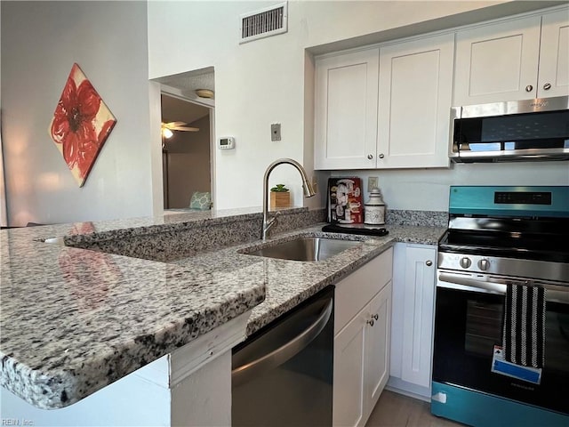 kitchen with stainless steel appliances, white cabinetry, light stone countertops, sink, and kitchen peninsula