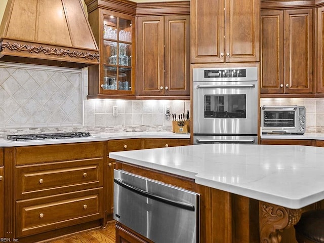 kitchen with tasteful backsplash, appliances with stainless steel finishes, premium range hood, and light stone counters