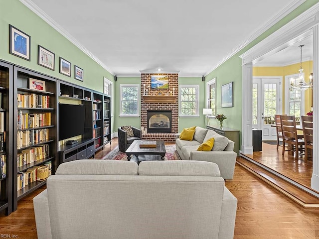 living room featuring a brick fireplace, hardwood / wood-style floors, crown molding, and an inviting chandelier