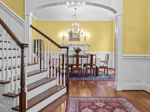 dining room with wood-type flooring, an inviting chandelier, crown molding, and decorative columns