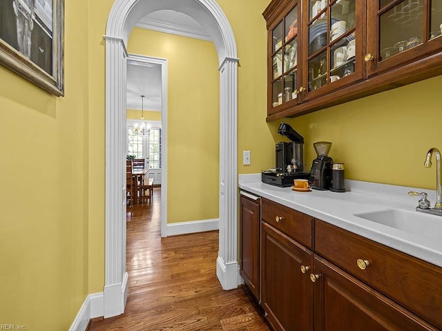 bar with dark wood-type flooring, a chandelier, sink, and crown molding