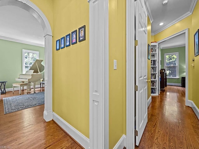 hall with wood-type flooring, a healthy amount of sunlight, and crown molding