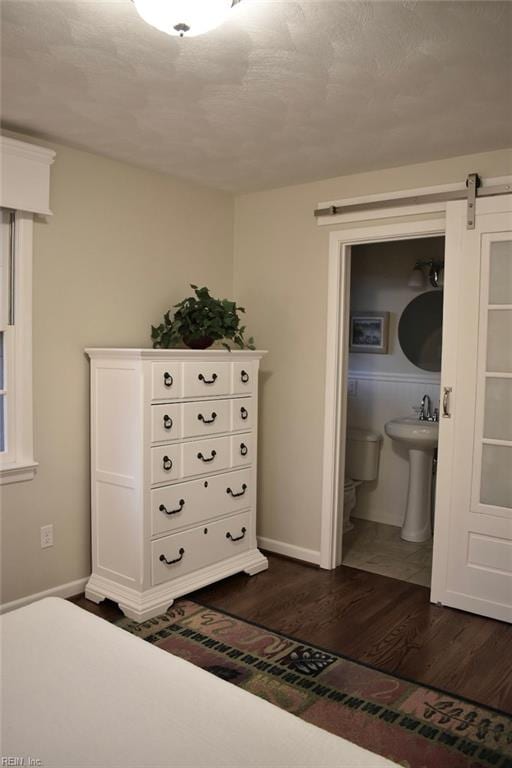 unfurnished bedroom with dark wood-type flooring, sink, a barn door, and ensuite bath