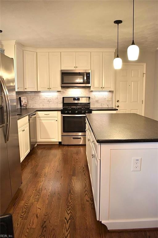 kitchen featuring white cabinetry, decorative backsplash, appliances with stainless steel finishes, pendant lighting, and dark hardwood / wood-style flooring