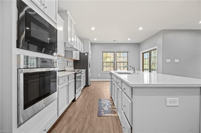 kitchen featuring light wood-type flooring, white cabinetry, appliances with stainless steel finishes, sink, and a kitchen island with sink