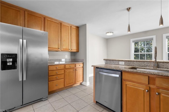 kitchen featuring appliances with stainless steel finishes, light tile patterned floors, pendant lighting, light stone countertops, and sink