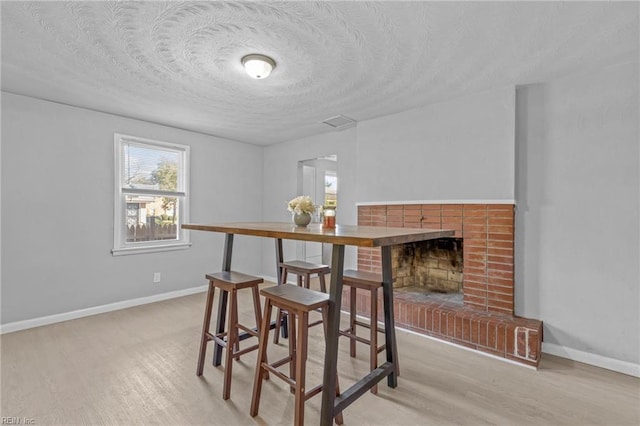 dining space featuring a fireplace, light hardwood / wood-style flooring, and a textured ceiling