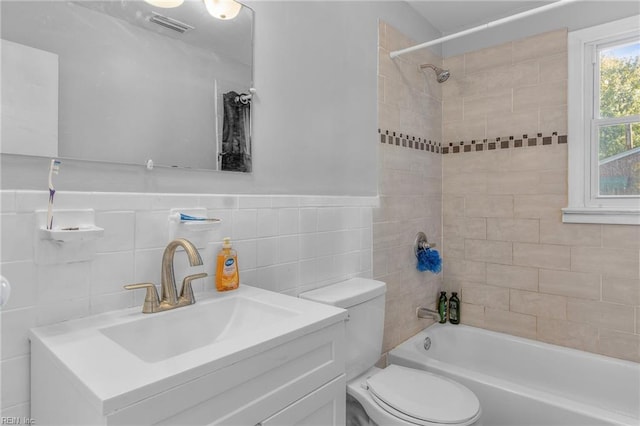 full bathroom with vanity, tiled shower / bath, toilet, and tile walls