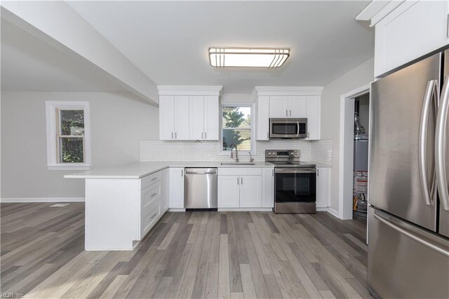 kitchen with white cabinetry, kitchen peninsula, appliances with stainless steel finishes, and light wood-type flooring