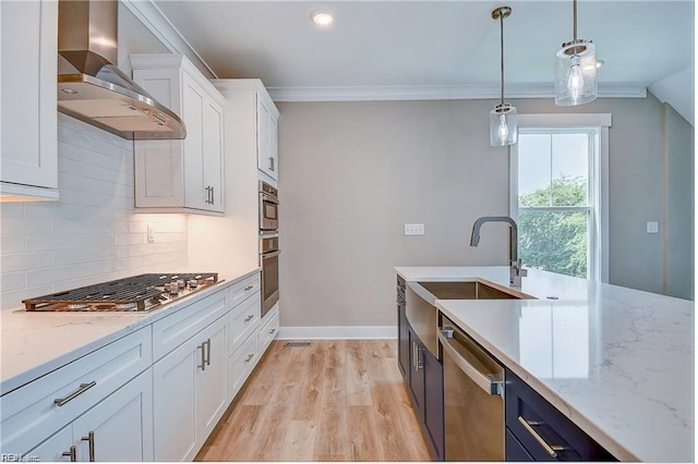 kitchen with light stone counters, stainless steel appliances, hanging light fixtures, white cabinets, and wall chimney exhaust hood