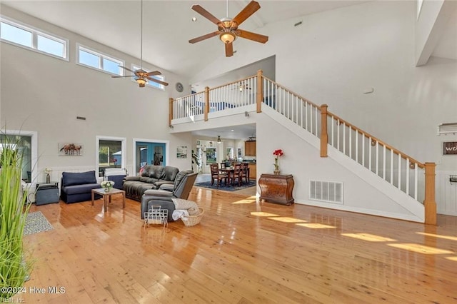 living room with a towering ceiling, light hardwood / wood-style flooring, a healthy amount of sunlight, and ceiling fan