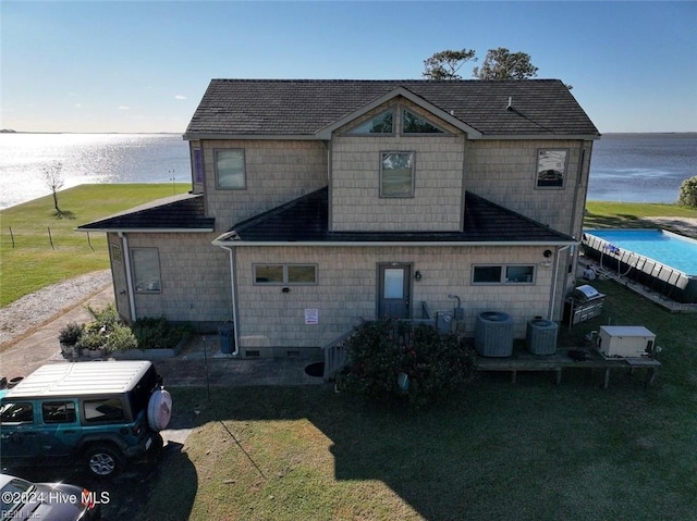 rear view of property with central AC unit, a lawn, and a water view