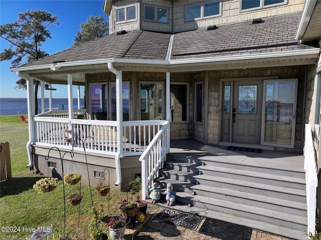 doorway to property with a porch, a water view, and a lawn