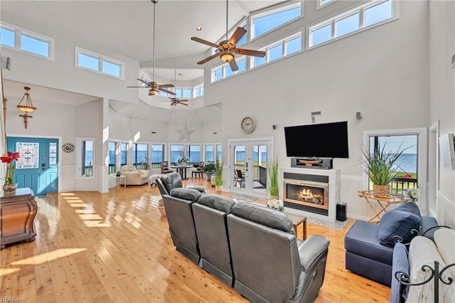 living room featuring light wood-type flooring, ceiling fan, a healthy amount of sunlight, and a towering ceiling