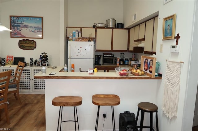 kitchen with kitchen peninsula, a breakfast bar, dark wood-type flooring, cream cabinetry, and white fridge