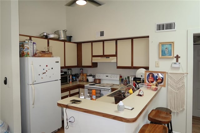 kitchen with sink, kitchen peninsula, wood-type flooring, white appliances, and a breakfast bar area