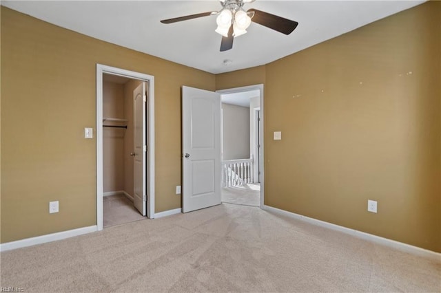 unfurnished bedroom with a closet, a spacious closet, light colored carpet, and ceiling fan