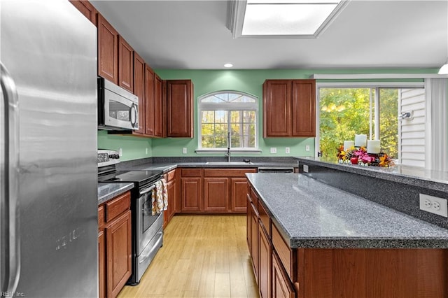 kitchen featuring dark stone countertops, light wood-type flooring, appliances with stainless steel finishes, and sink