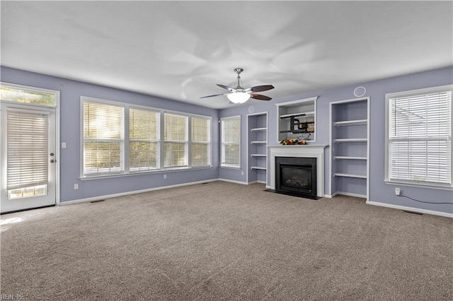 unfurnished living room featuring built in shelves, carpet floors, and ceiling fan